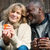 A happy couple sitting close together, both holding mugs