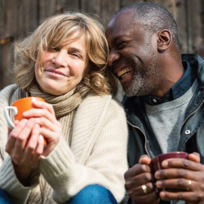 A happy couple sitting close together, both holding mugs