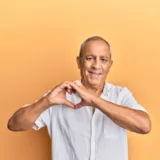 An older male adult making a heart sign with his hands